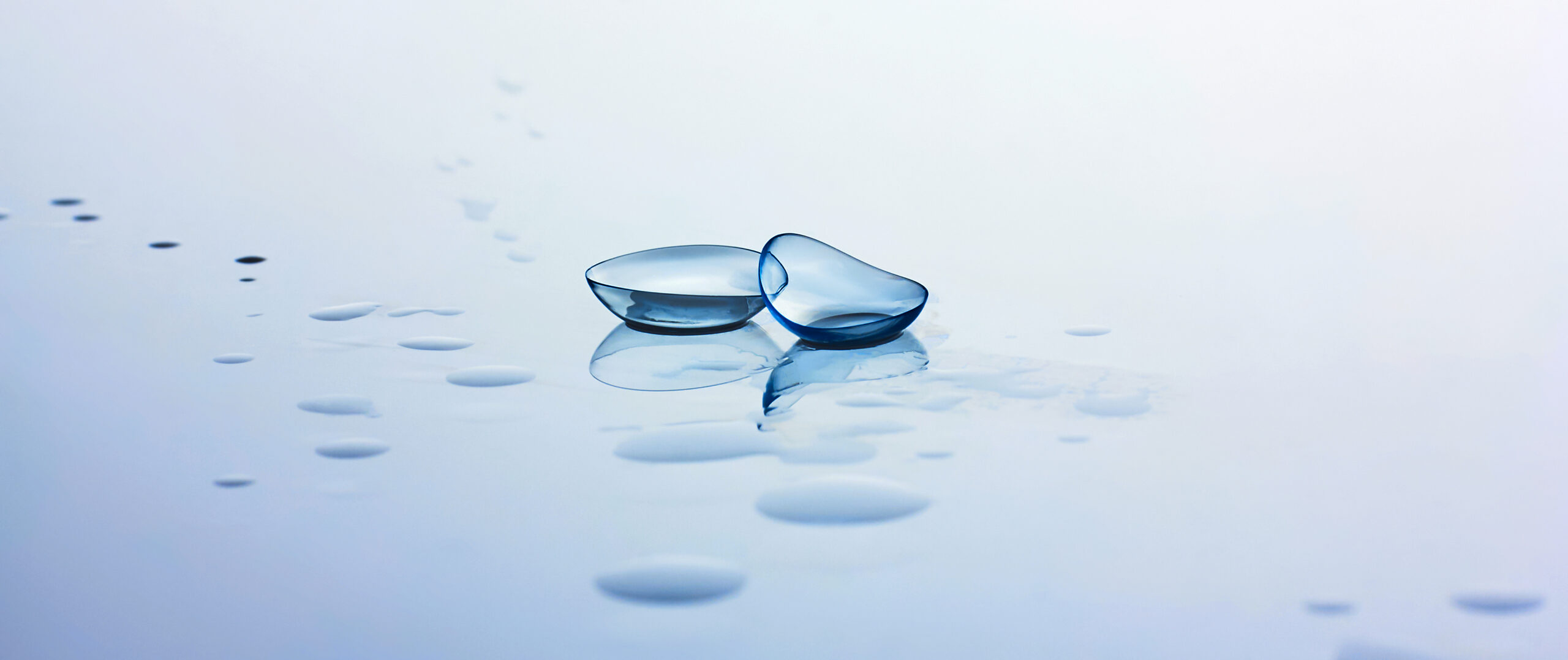 Contact lenses and water drops on light blue background